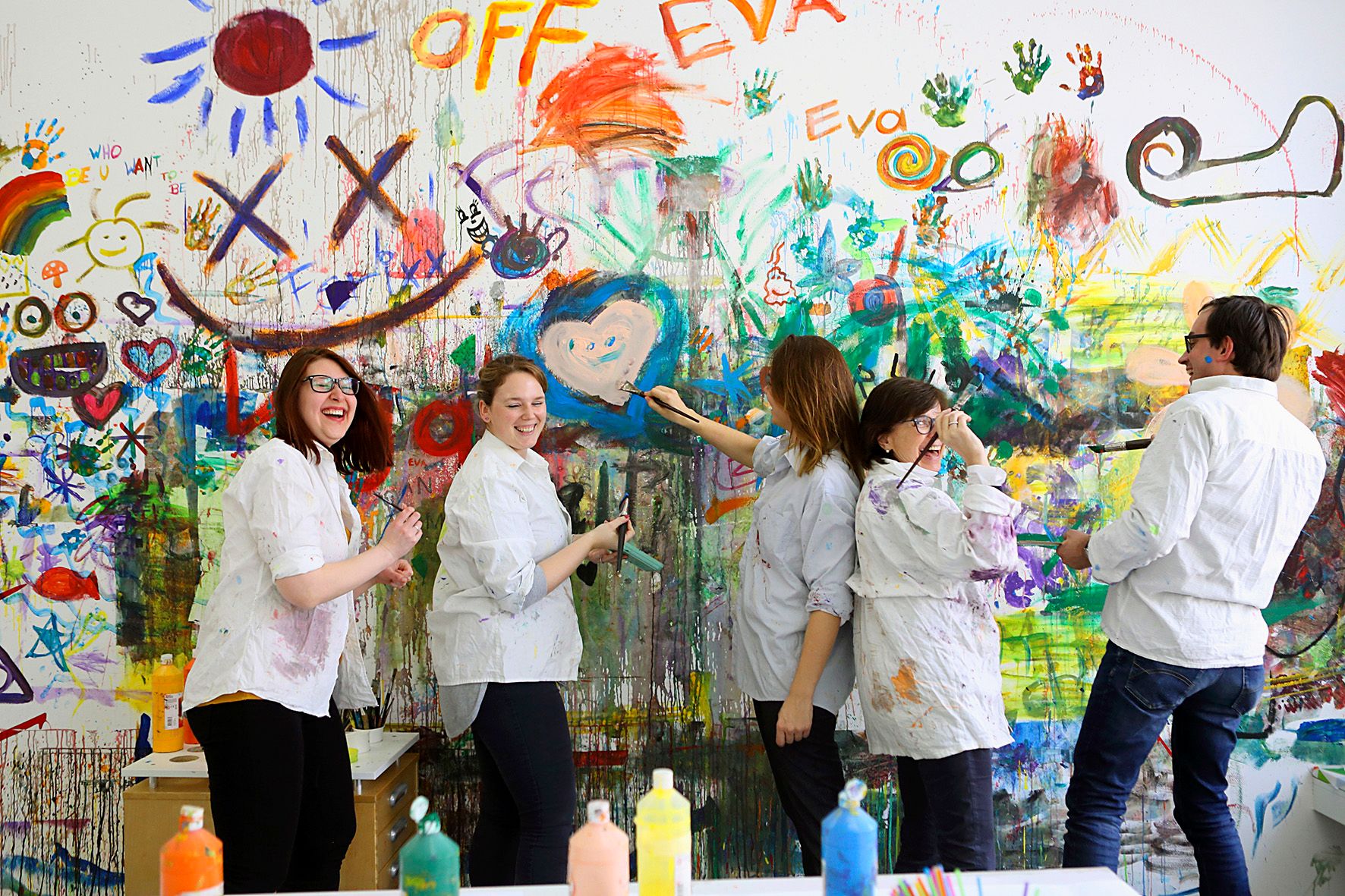 Group of people happily painting on a colorful wall.