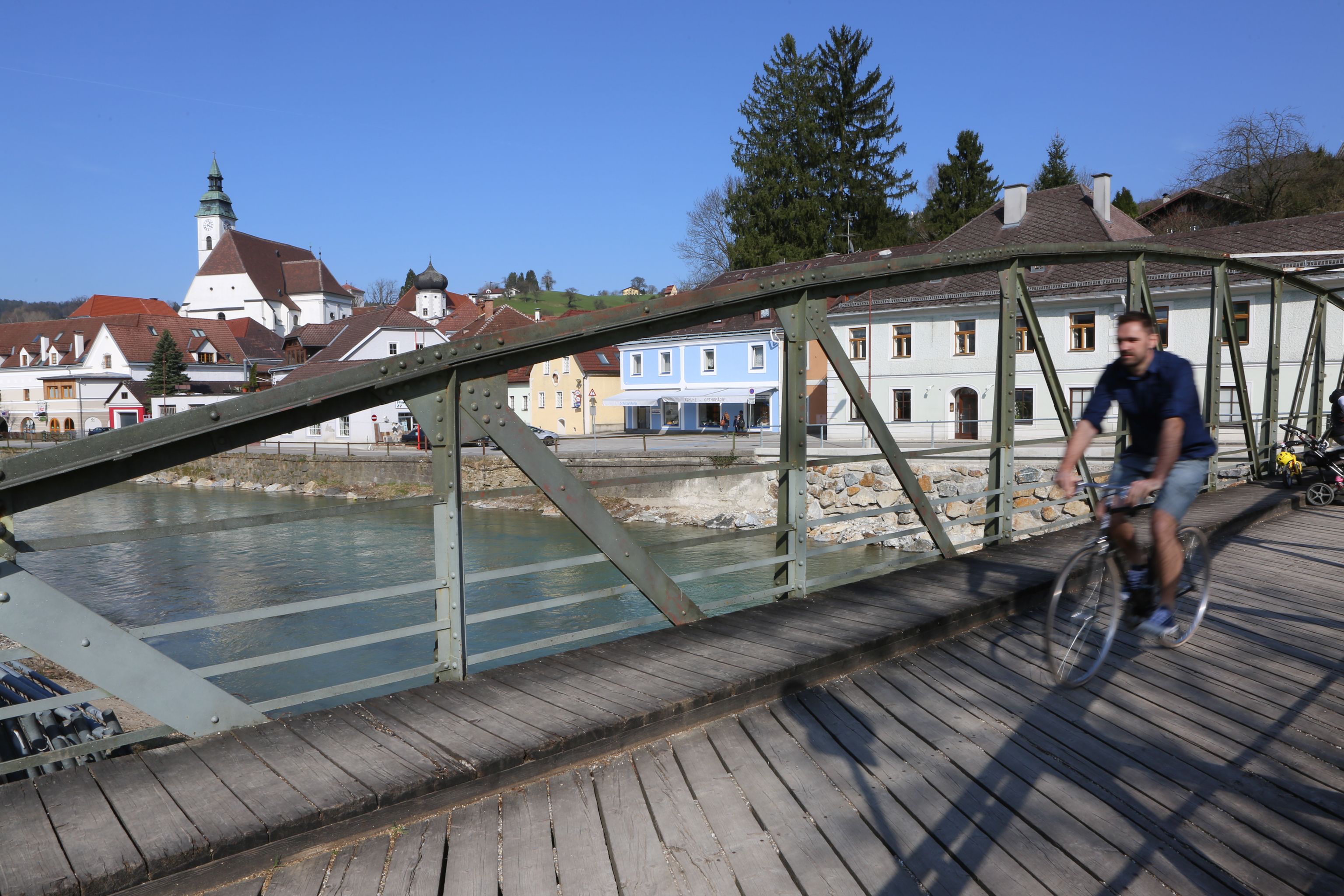 A cyclist crosses the Töpper Bridge in a picturesque town with a church and colorful houses in the background.