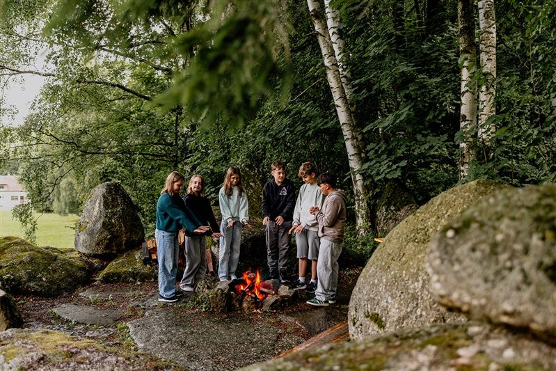 Group of young people standing around a campfire in the forest.
