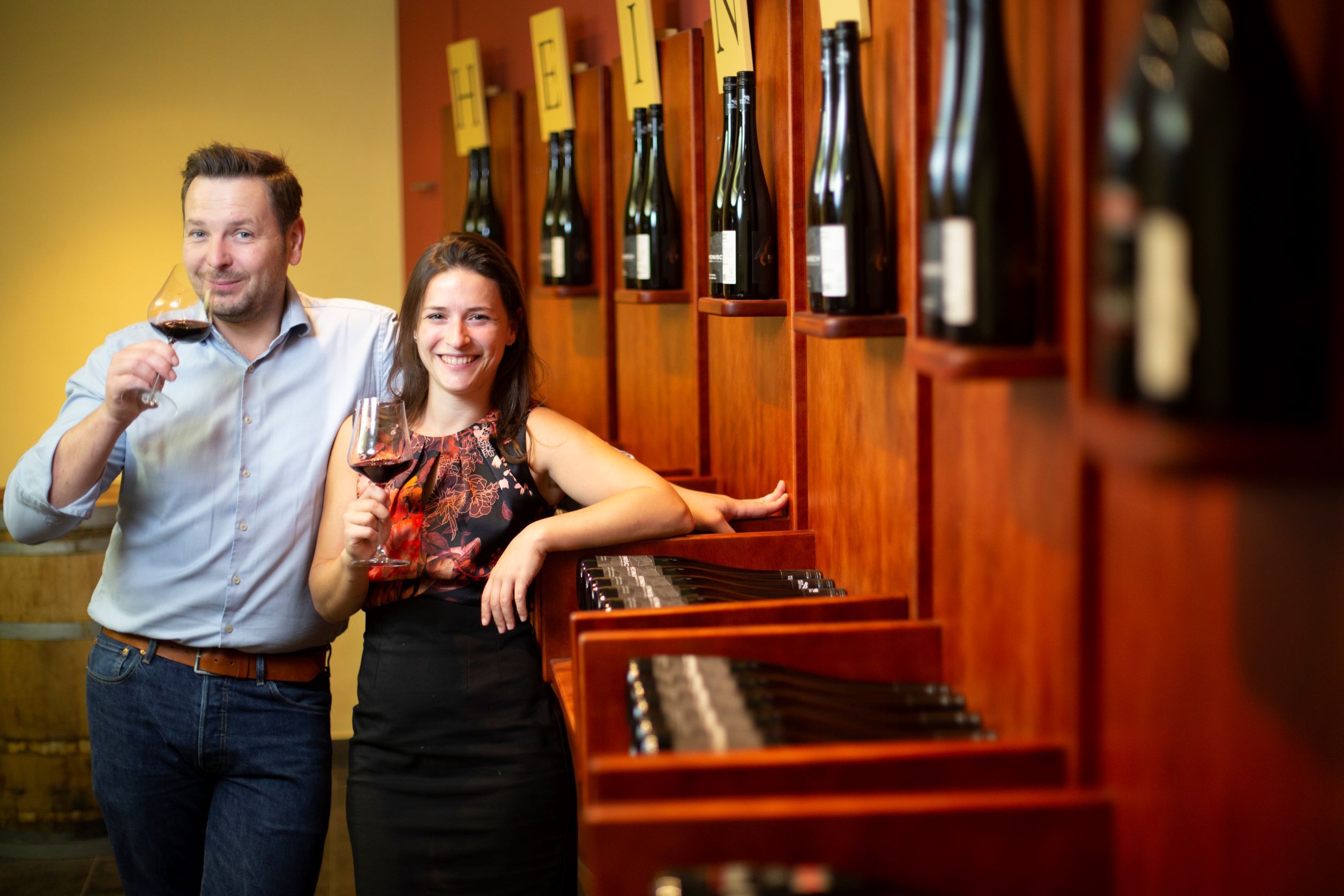 Two people in a wine cellar with wine glasses in their hands.