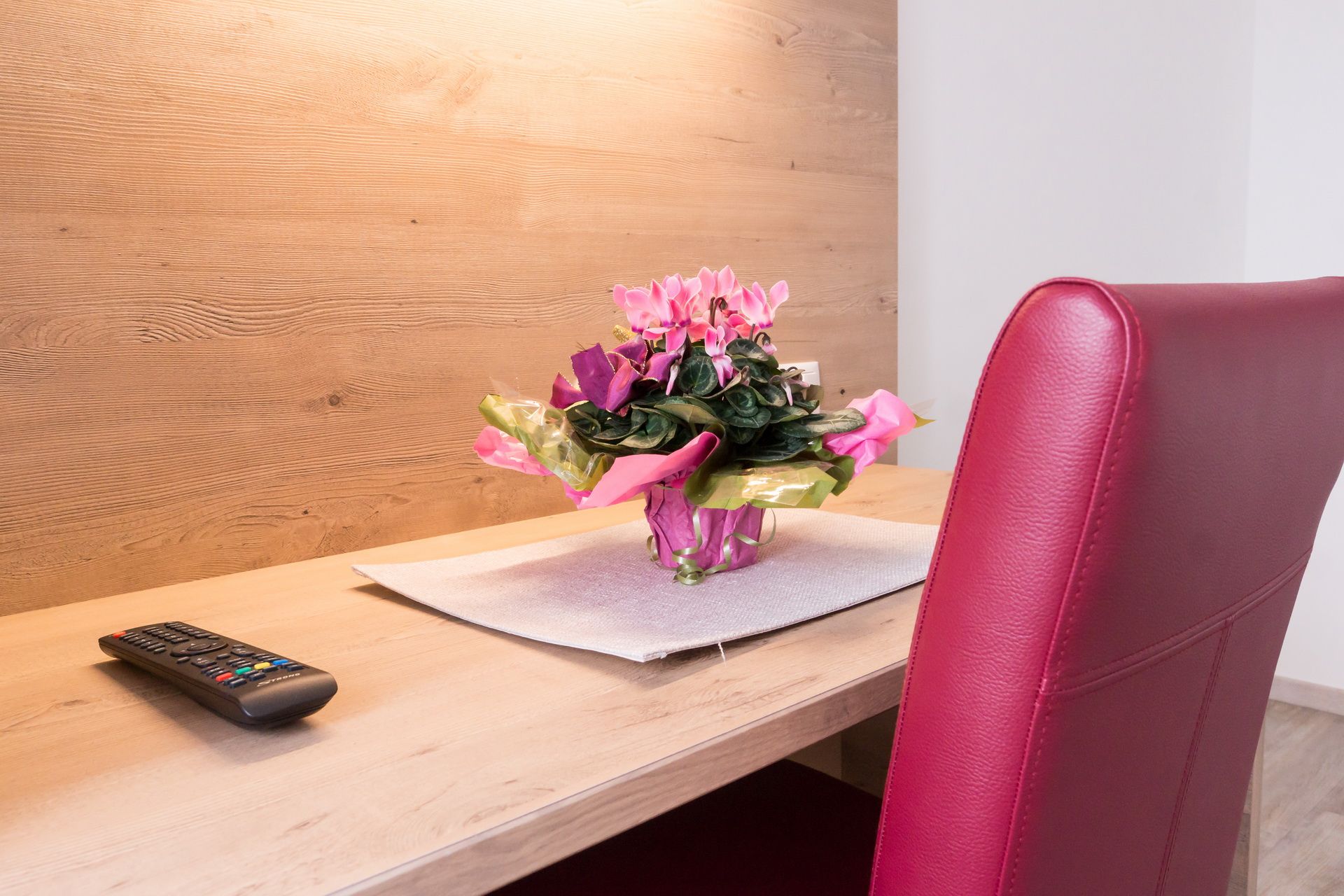 A desk with a remote control, a bouquet of flowers and a red chair.