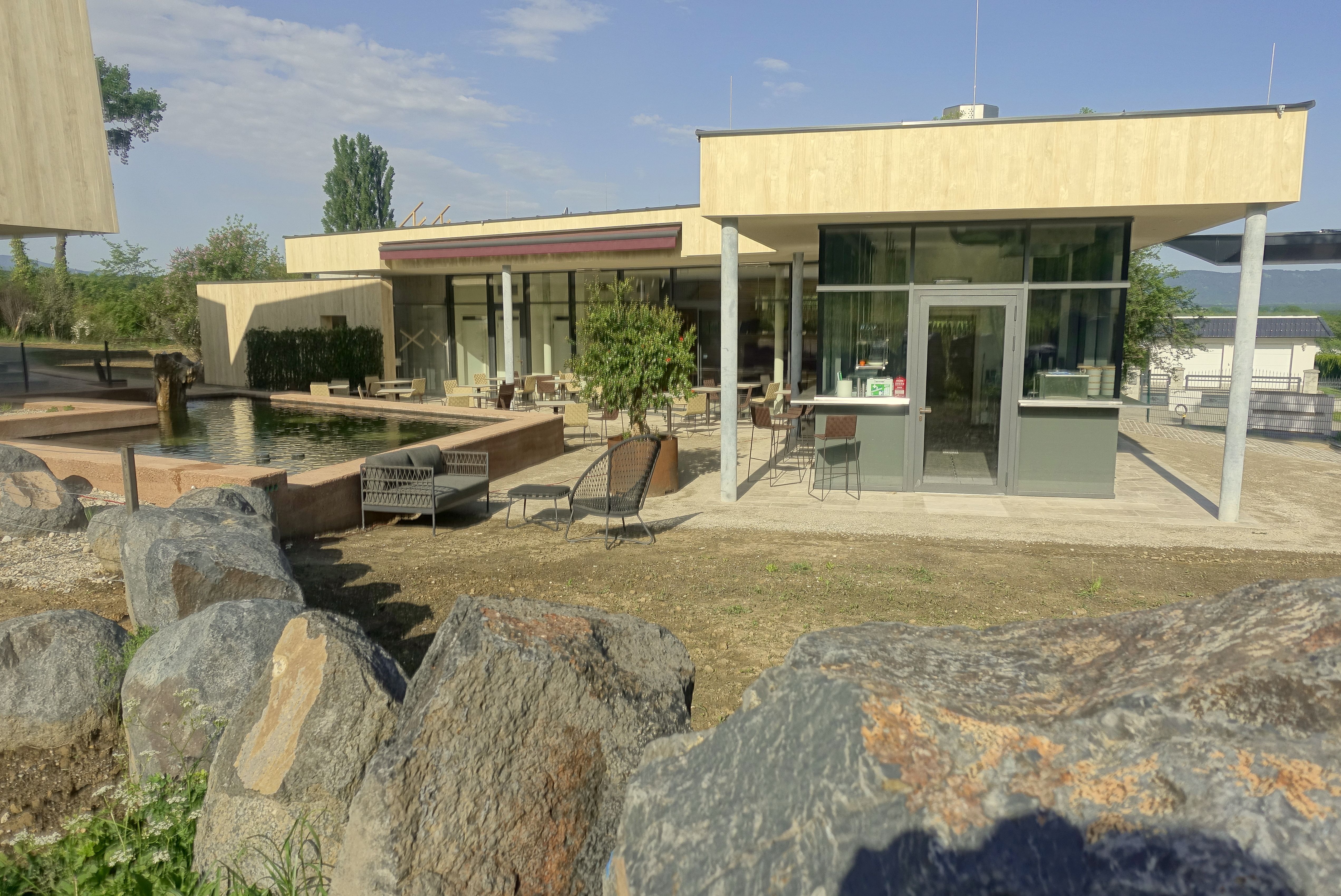 Modern veranda with glass front and seating area, surrounded by rocks and a pond.