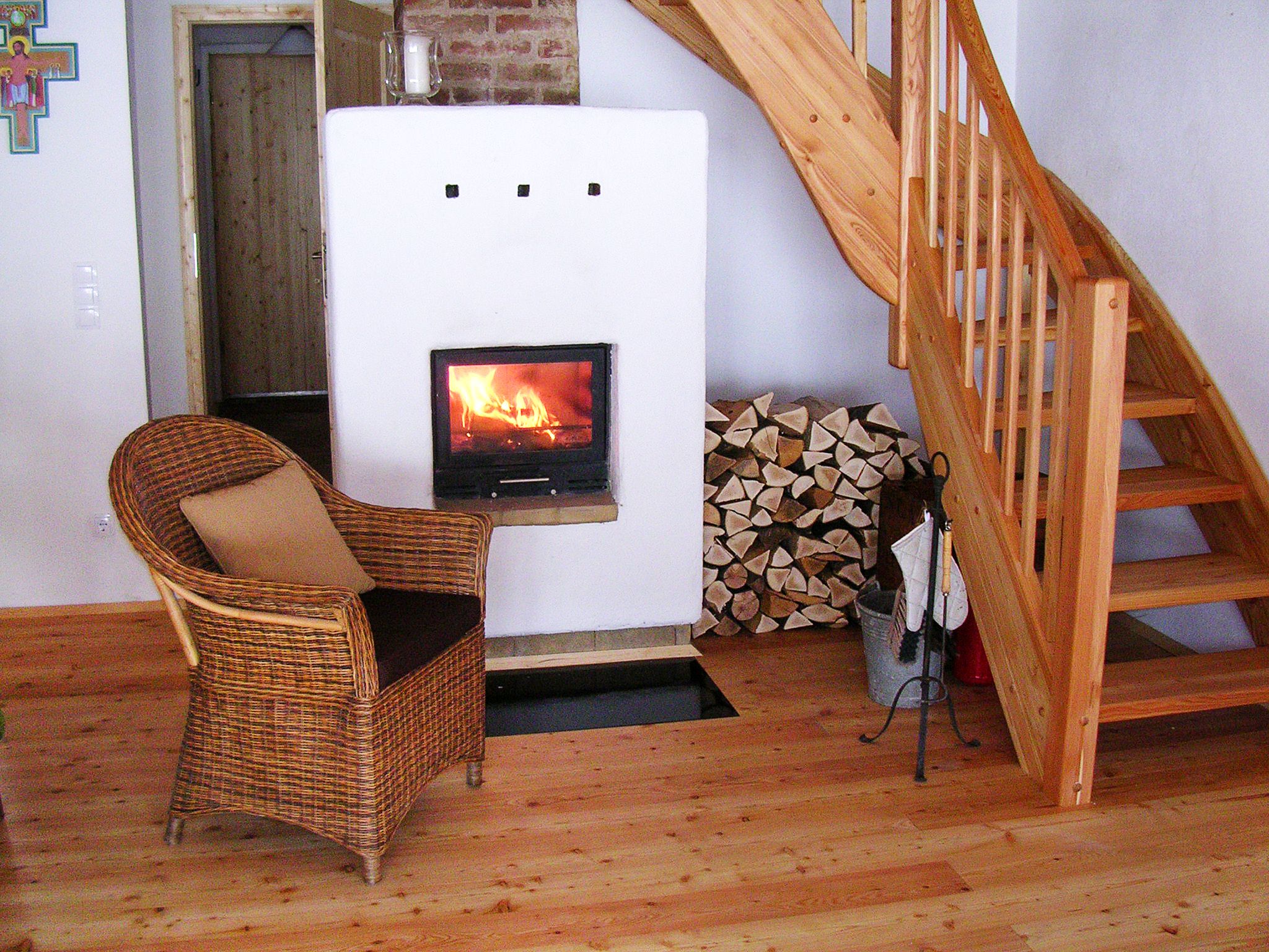 Interior of a vacation home with fireplace, wood pile, wicker armchair and wooden staircase.