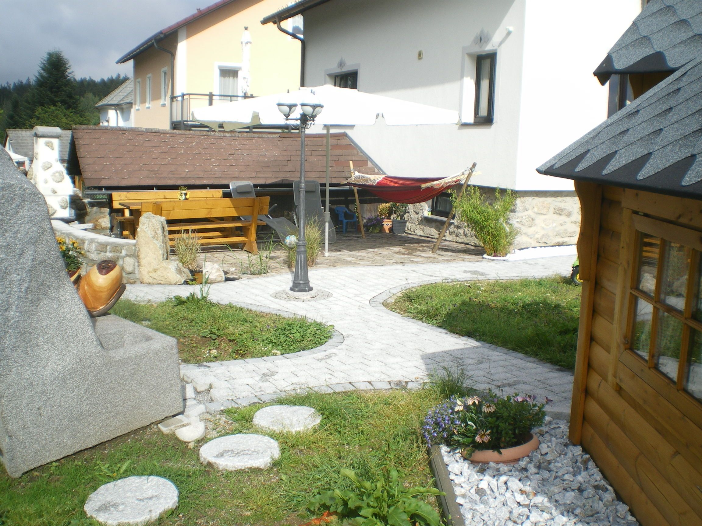 Garden with stones, wooden house, table, hammock and parasol.
