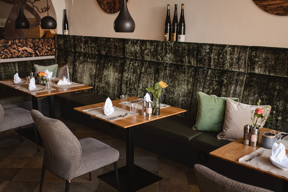 A modern restaurant with stylishly laid tables, upholstered benches and wine bottles as decoration.