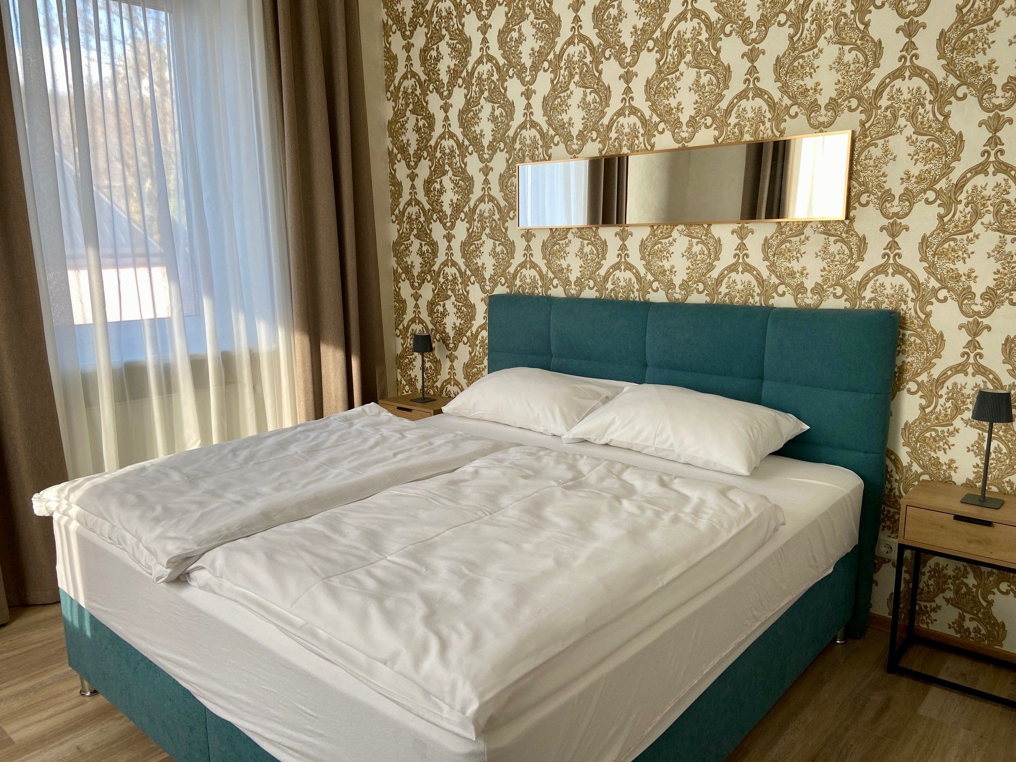 A stylishly furnished bedroom with a large bed, blue headboard and golden wallpaper.