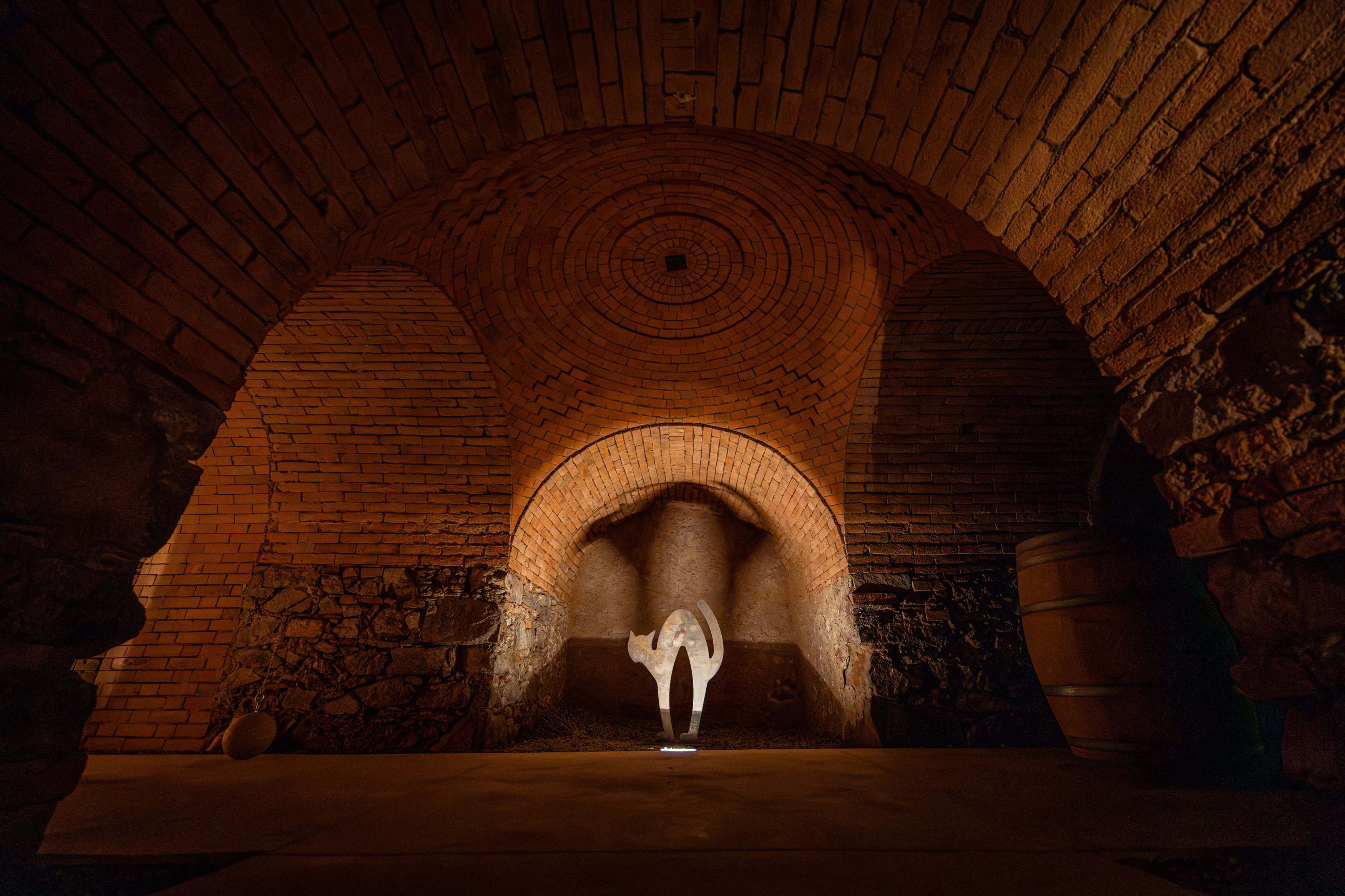 A wine cellar with brick walls and an illuminated work of art in the shape of a cat.
