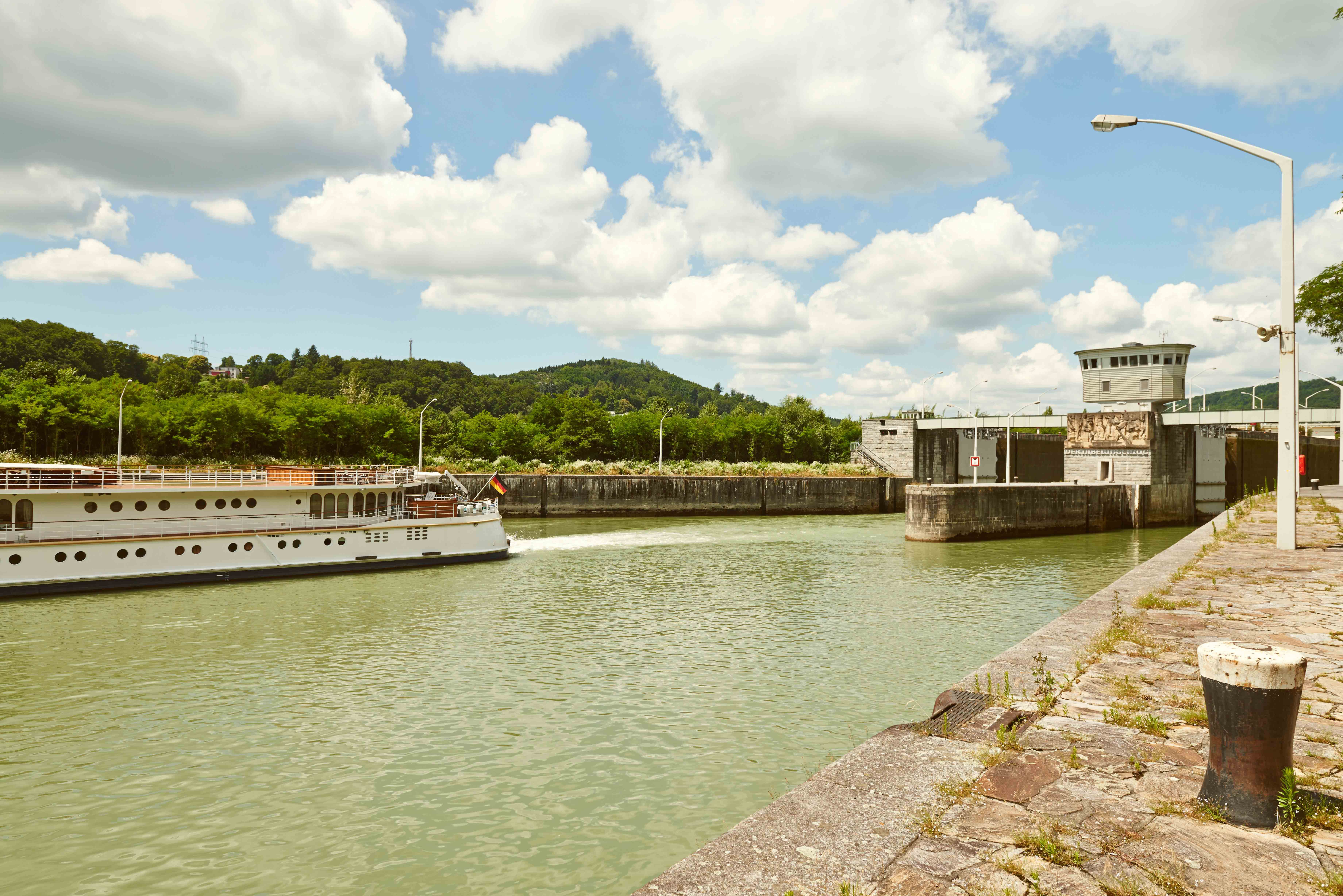 A ship passes through a lock at the Ybbs-Persenbeug Danube power station, surrounded by green countryside and a cloudy sky.