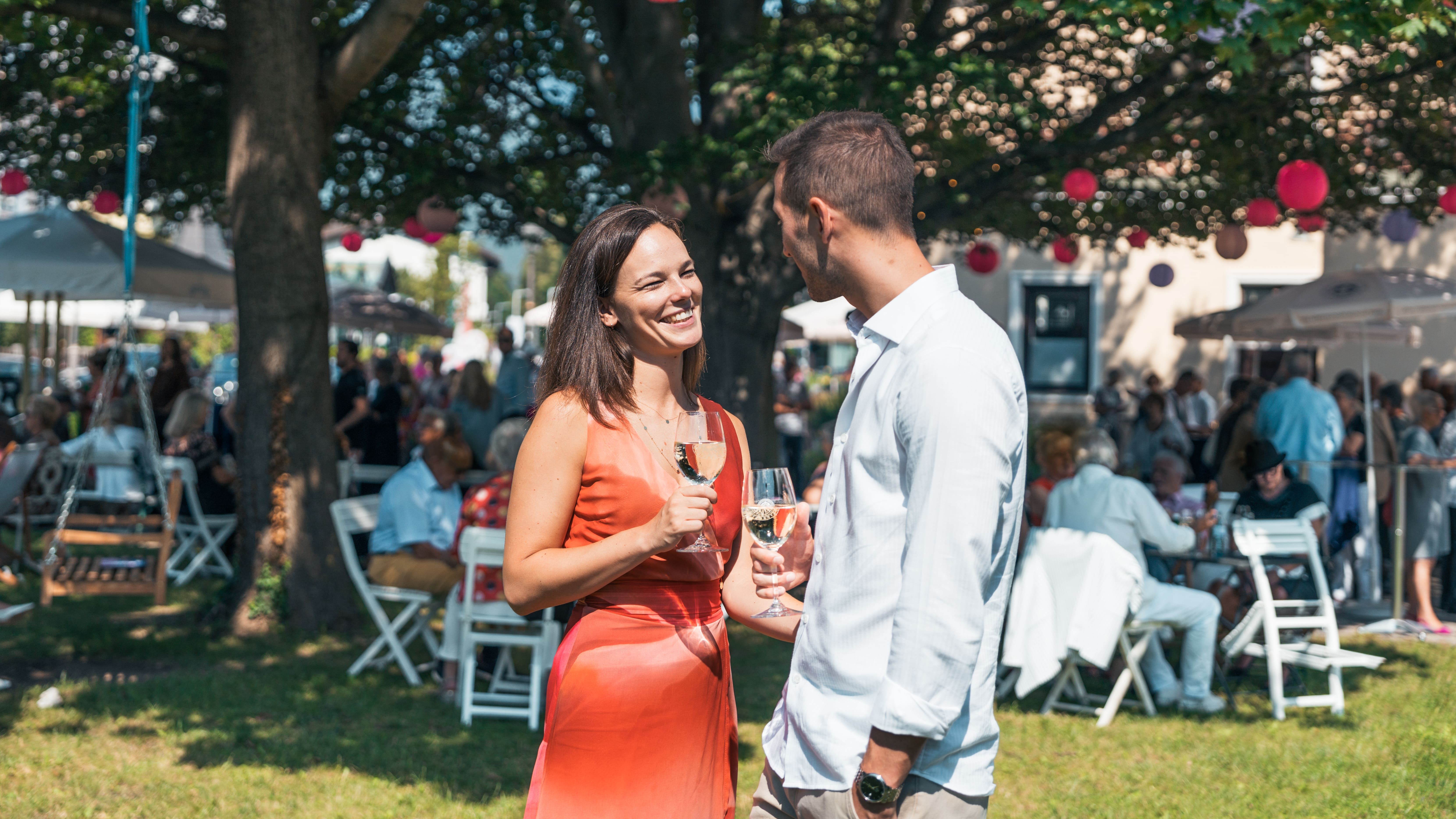 Two people outdoors with wine glasses in their hands.