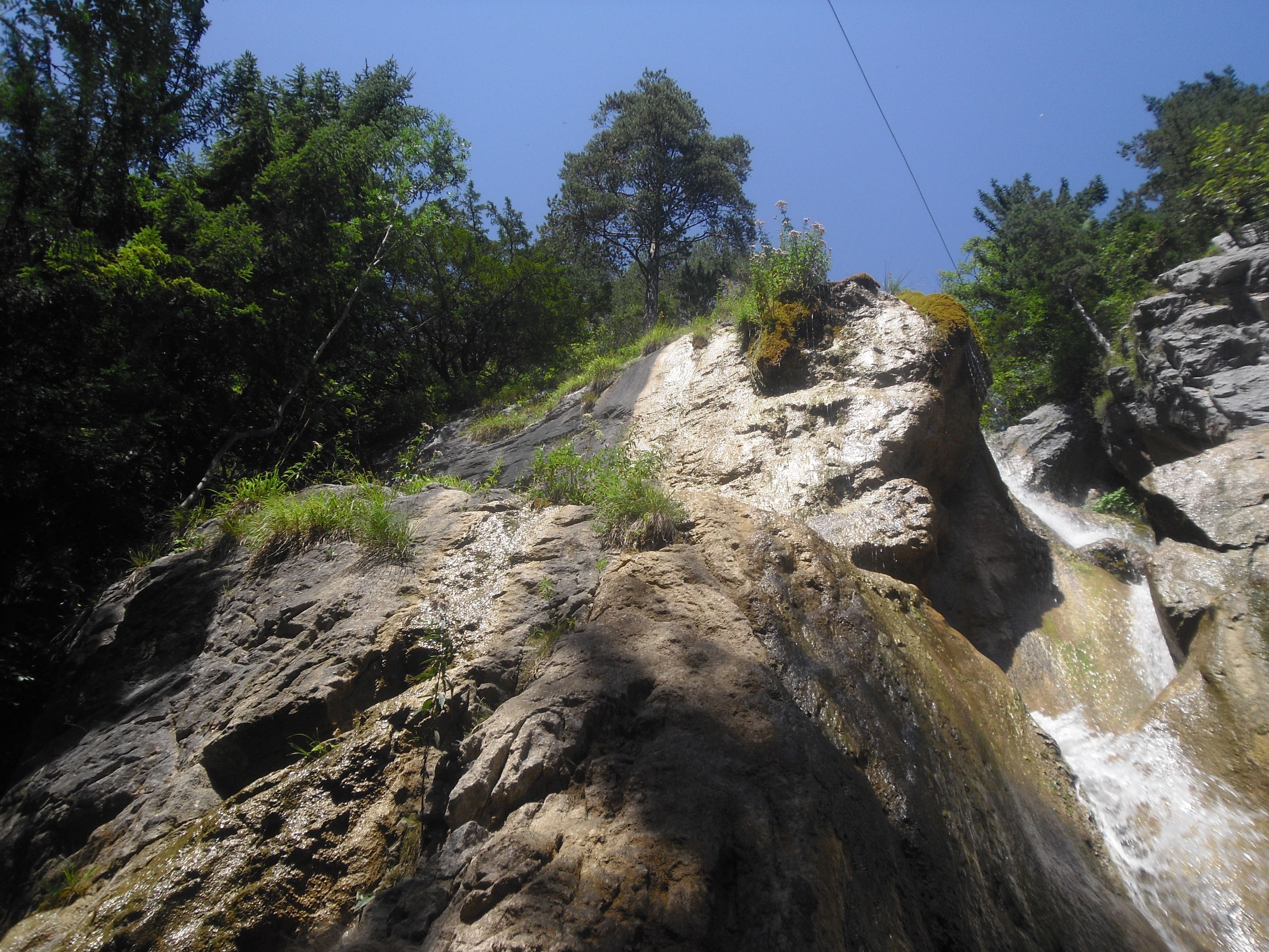 Rocky waterfall with trees and blue sky.