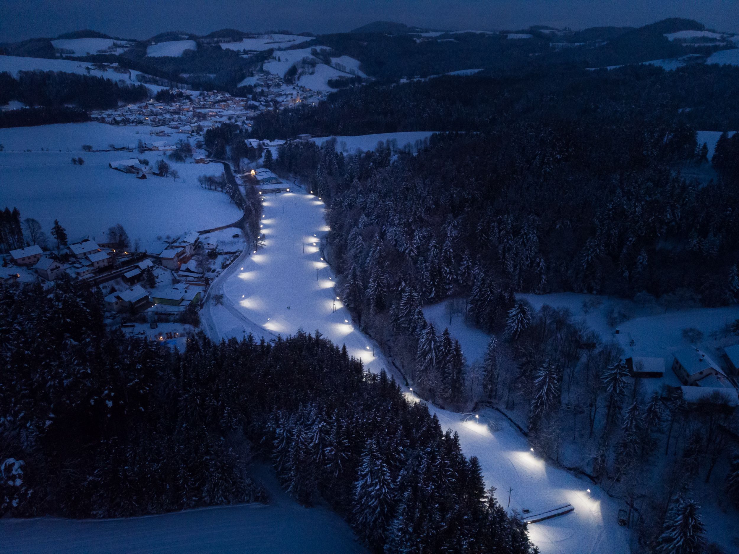 Aerial view of an illuminated cross-country ski trail in a snowy landscape at night.