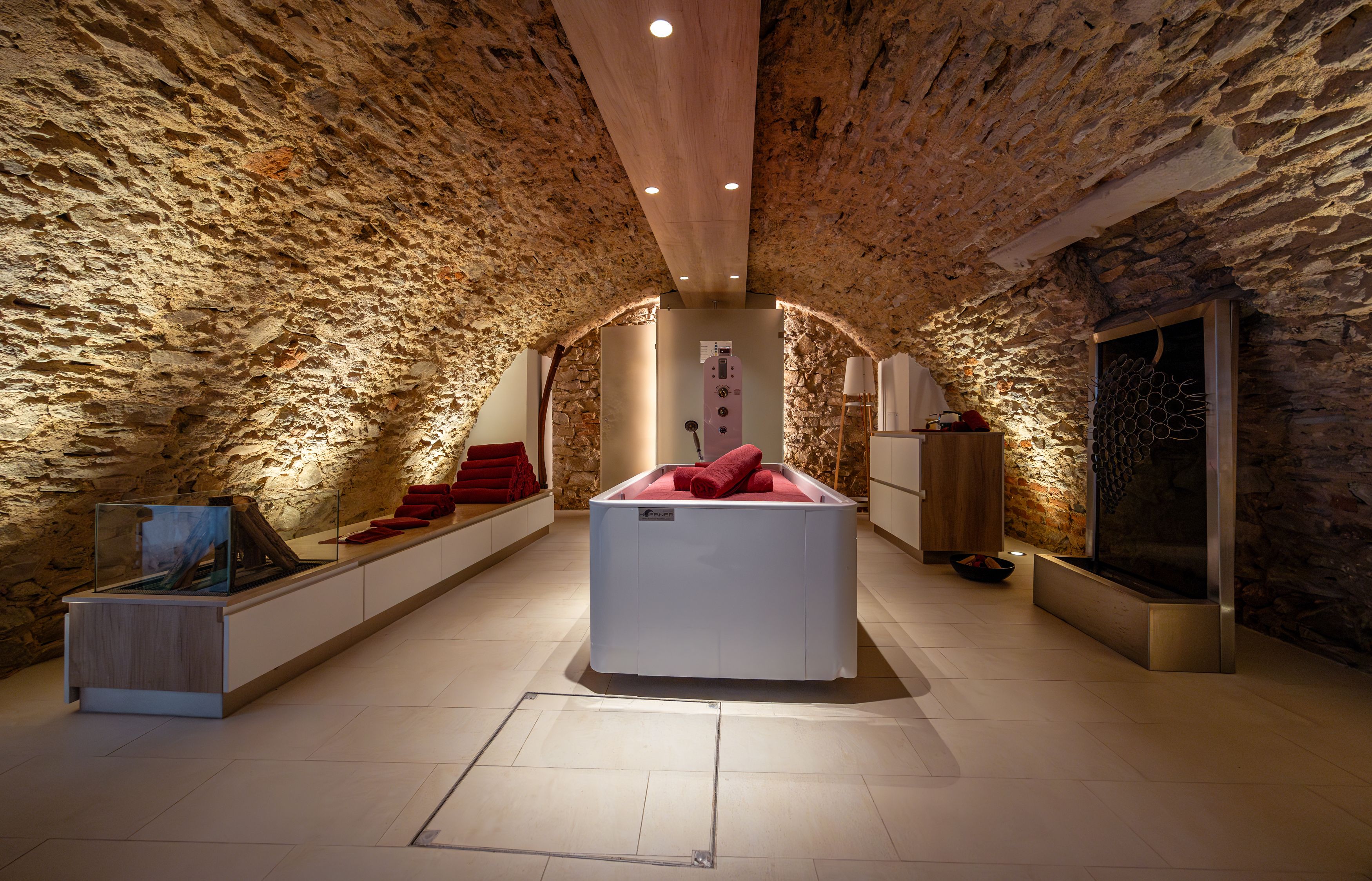 A stylish spa room with stone walls, a modern bathtub and red towels.