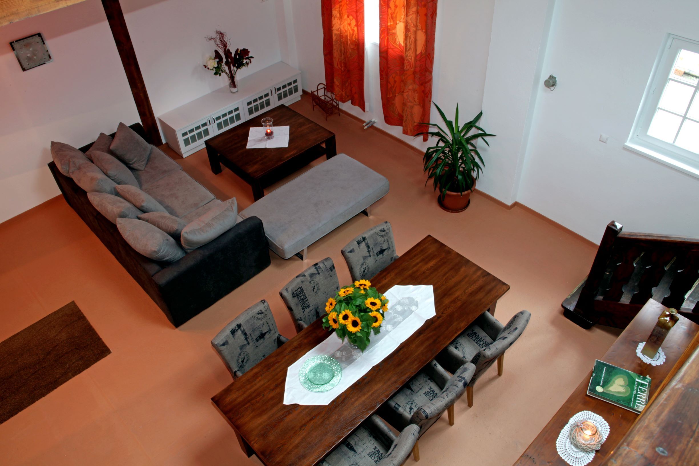 View from above of a living room with a gray sofa, dining table with sunflowers, red curtains and a plant.
