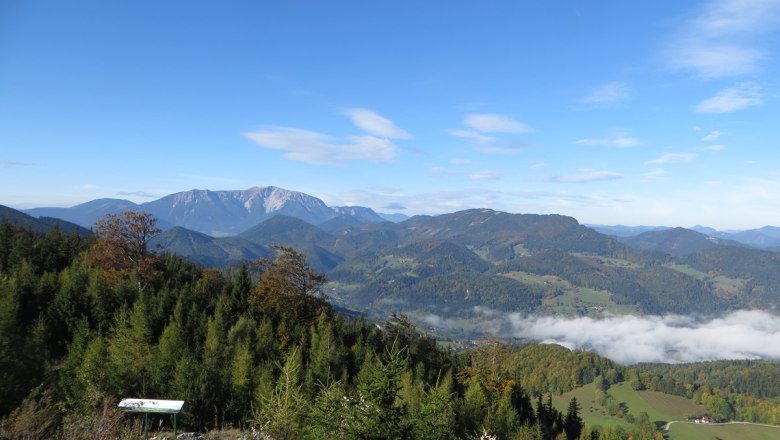 Panoramic view of wooded hills and mountains under a blue sky with scattered clouds.