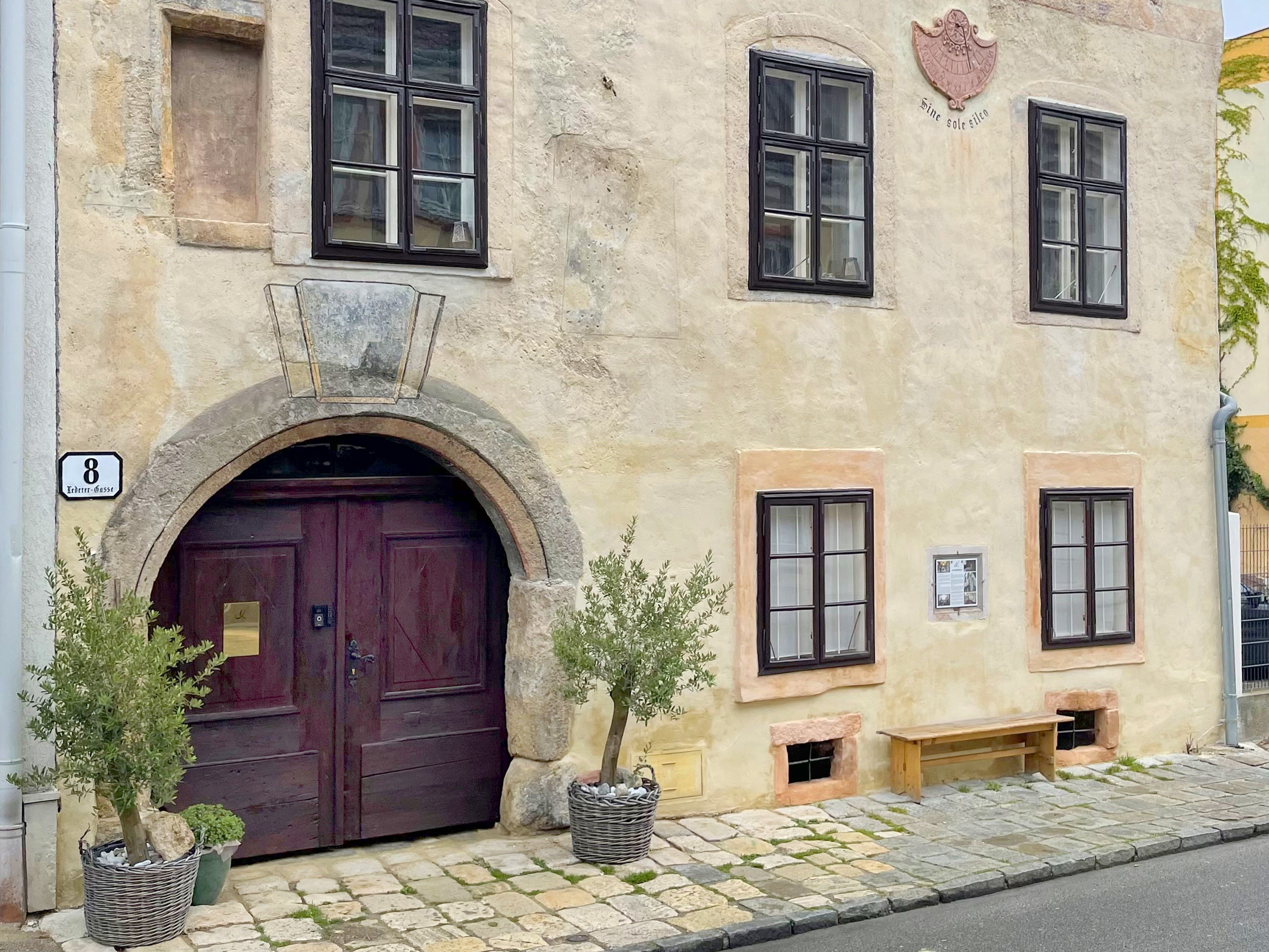 Historic house facade with wooden gate and windows, decorated with plants in baskets.