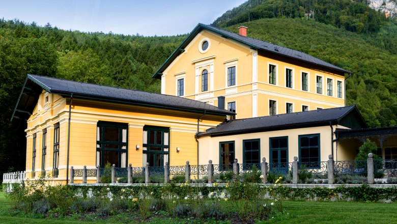 Thalhof exterior view, © Thalhof, Katrin Nusterer Exterior view of a yellow building with a garden and forest in the background.