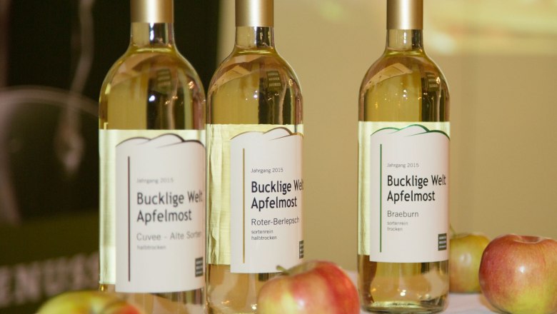 Three bottles of Bucklige Welt cider on a table with apples.