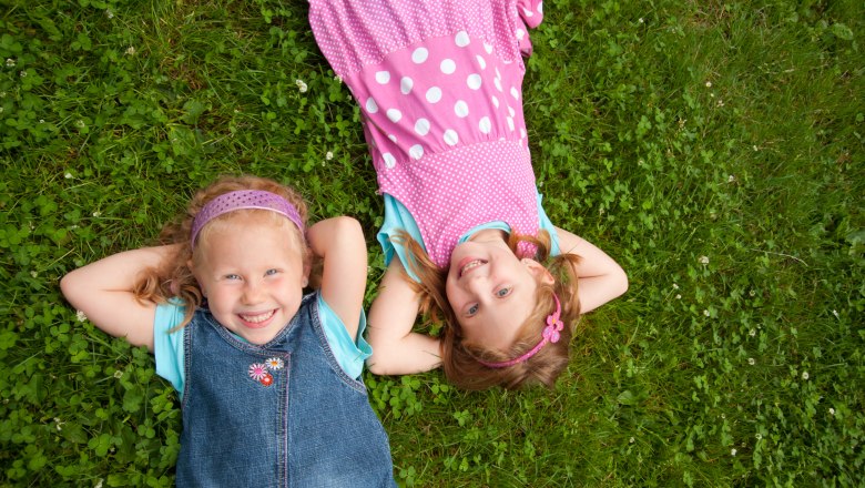 Two laughing girls lie on a meadow.