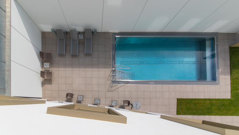 Top view of a rectangular pool with sun loungers and tables on a tiled terrace.