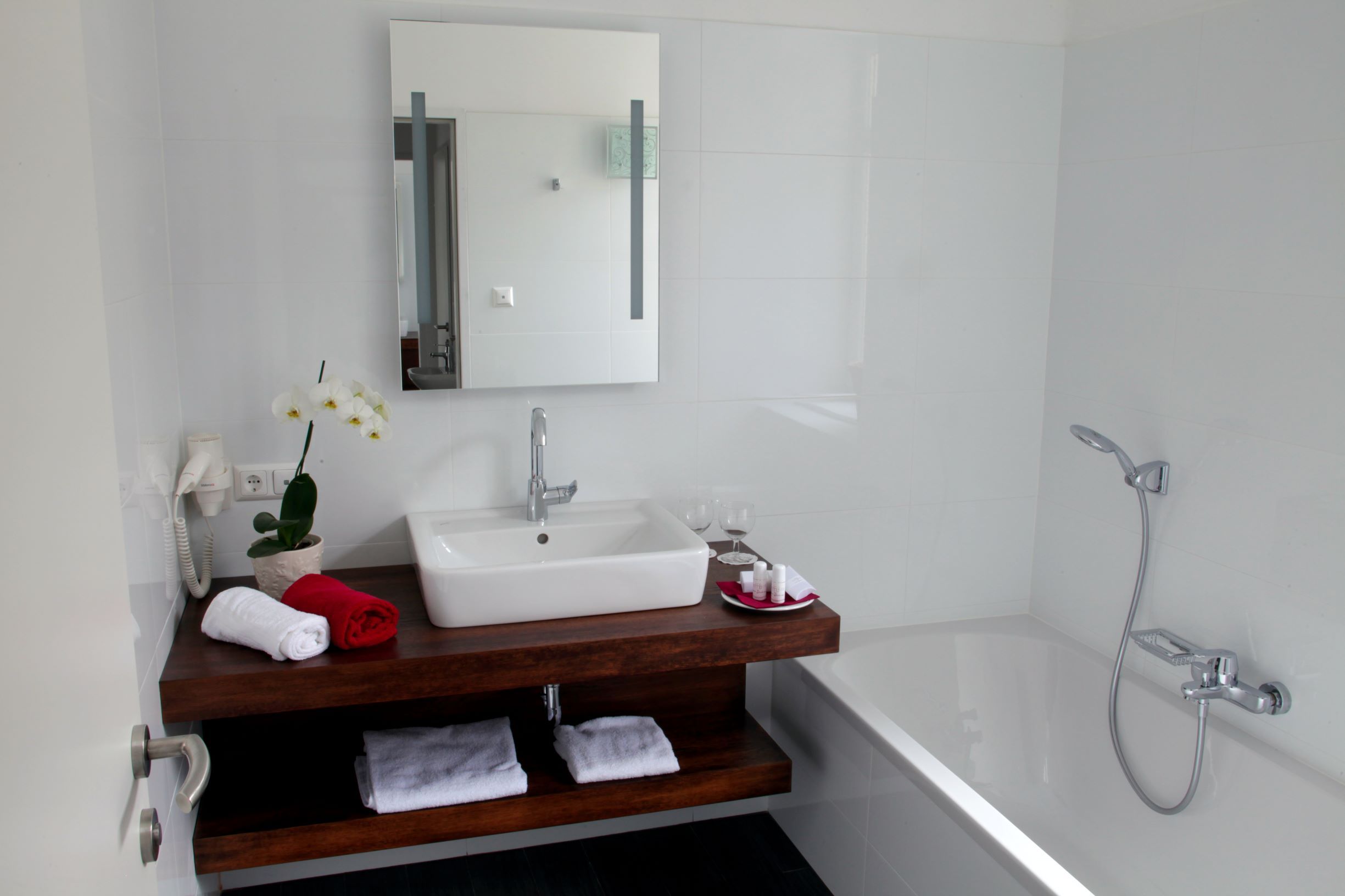 Modern bathroom with washbasin, mirror, bathtub and towels.