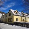 Yellow house with snow-covered roof in winter, blue sky.