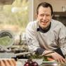 A chef in a white uniform smiles in a kitchen surrounded by fresh ingredients and a Wachau quality seal.