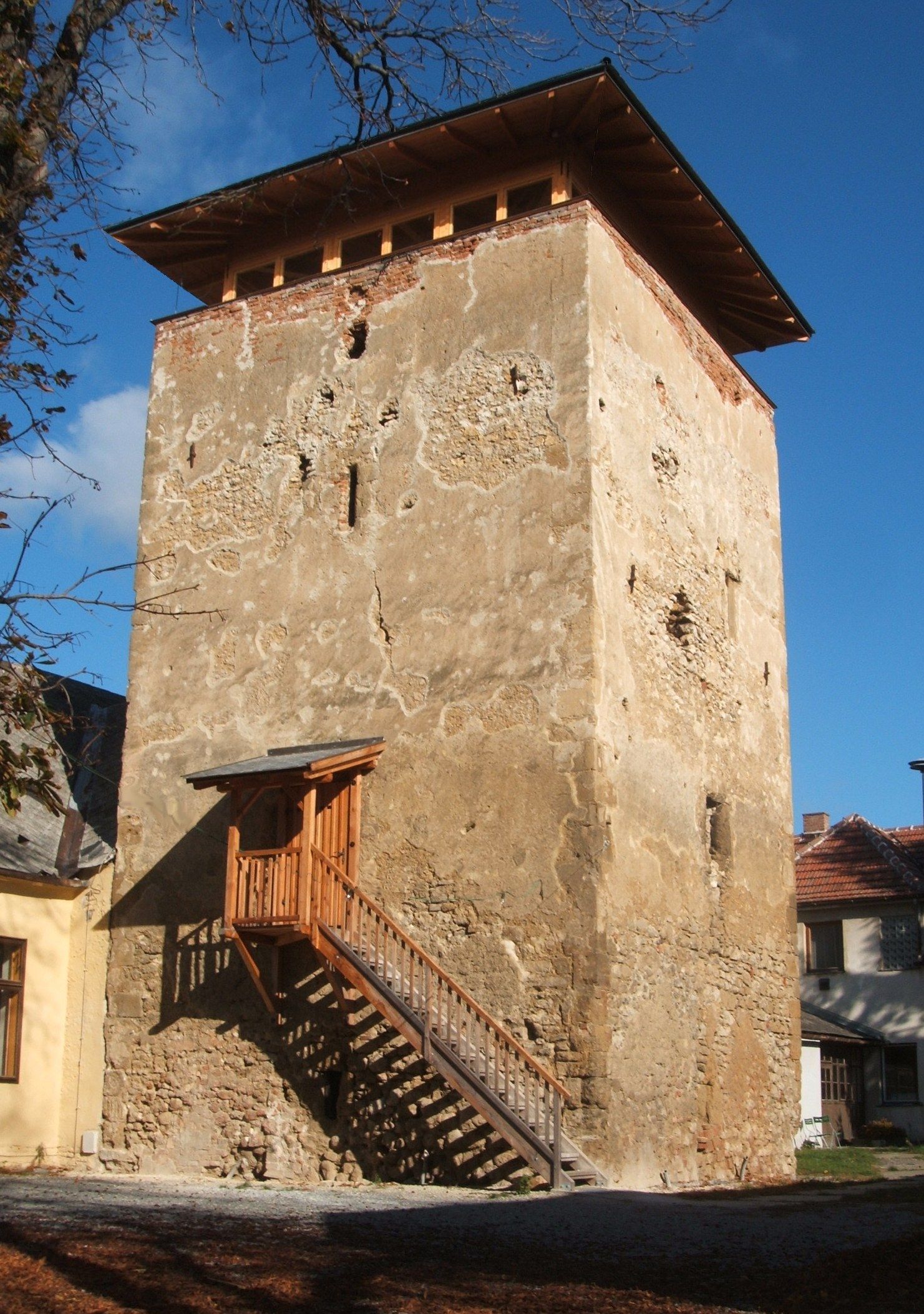 An old fortified tower with a crumbling façade and a wooden staircase on the side.