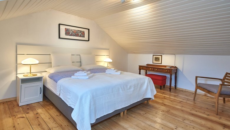 Cozy bedroom with double bed, wooden floor and sloping ceiling.