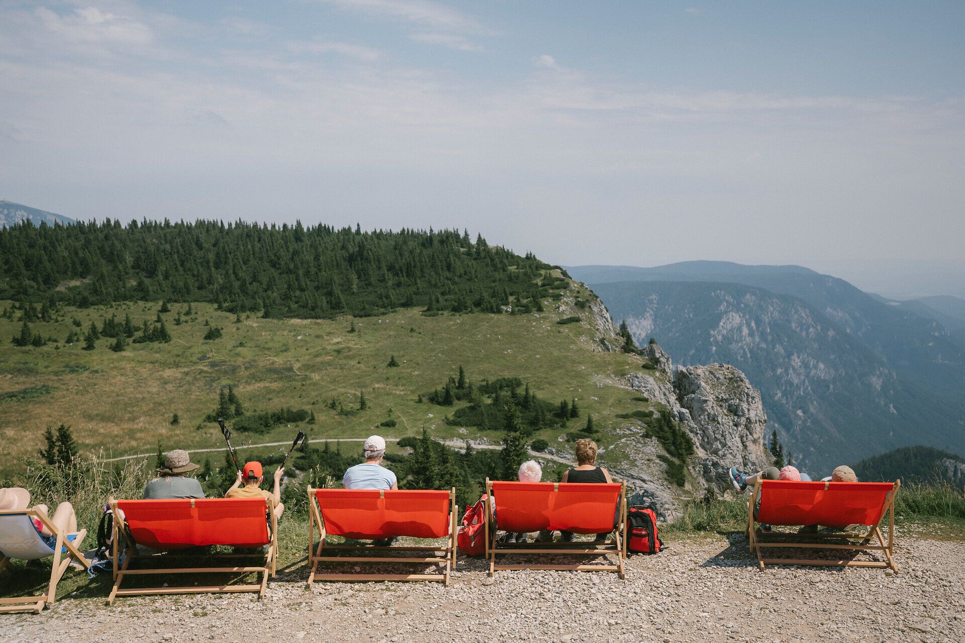 Guests relax in red lounge chairs overlooking the rock face near the Ottohaus on the Rax