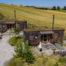 Two rustic wooden houses with green roofs in a rural setting.