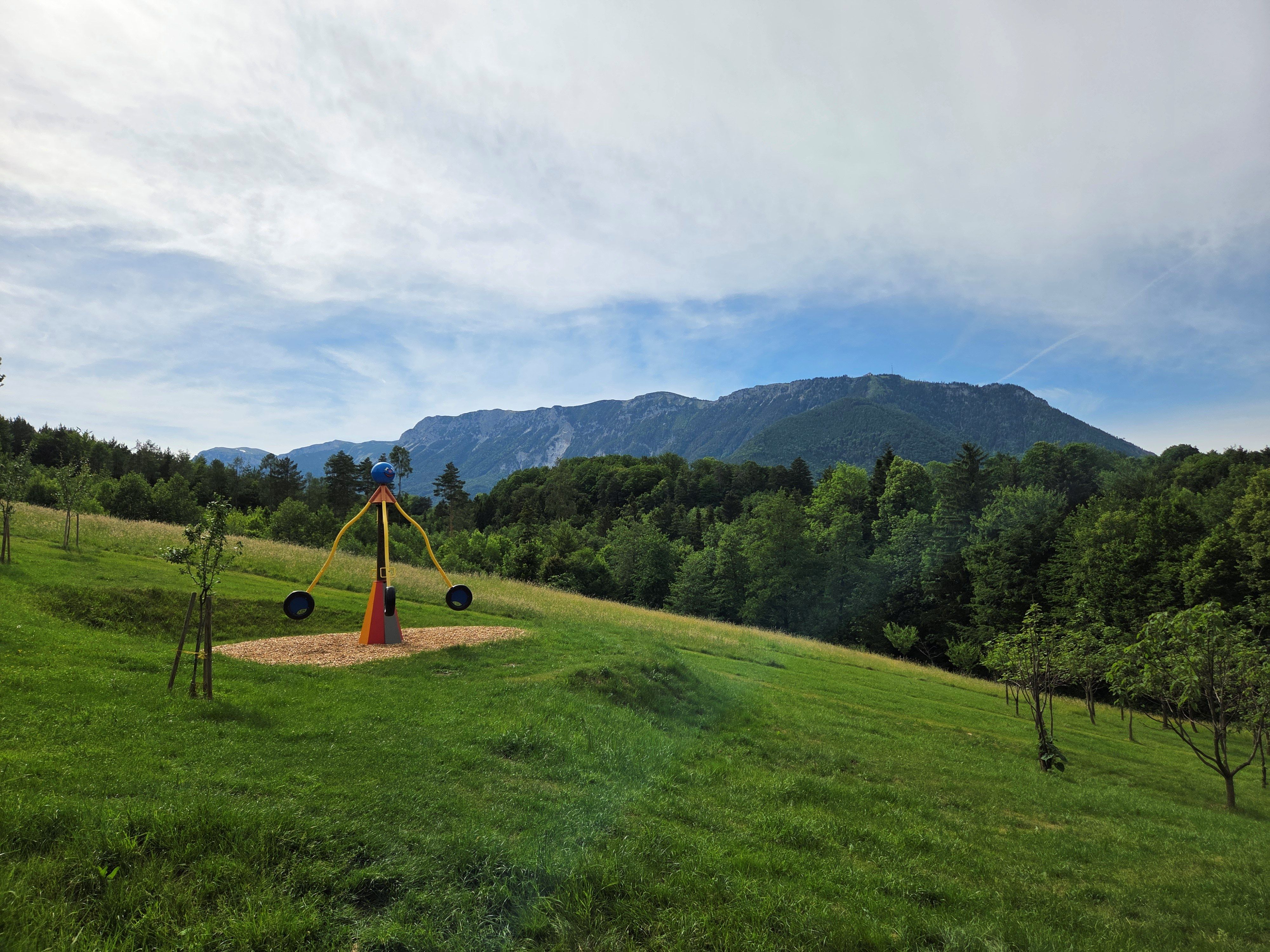 A children's playground with a seesaw set against a mountain landscape, with the Rax in the background.