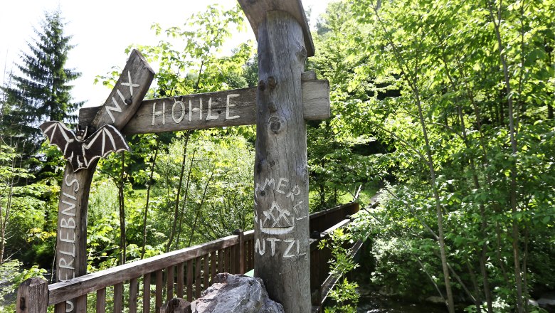 Entrance to the Nix Cave with wooden sign and bat decoration, surrounded by green vegetation.