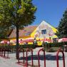 A yellow building with murals, surrounded by trees and red parasols.