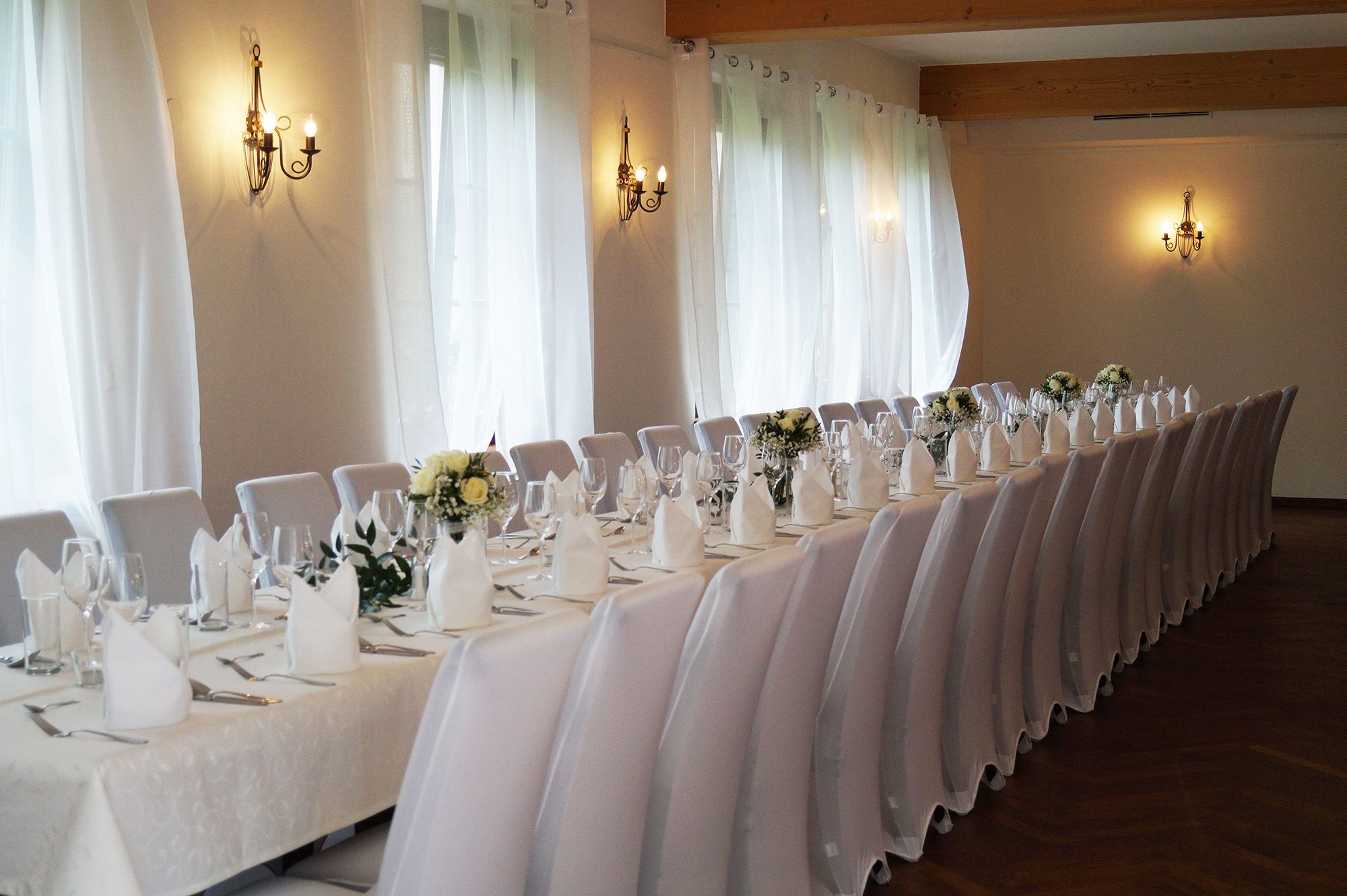 Elegant function room with long, festively laid tables and white chairs.