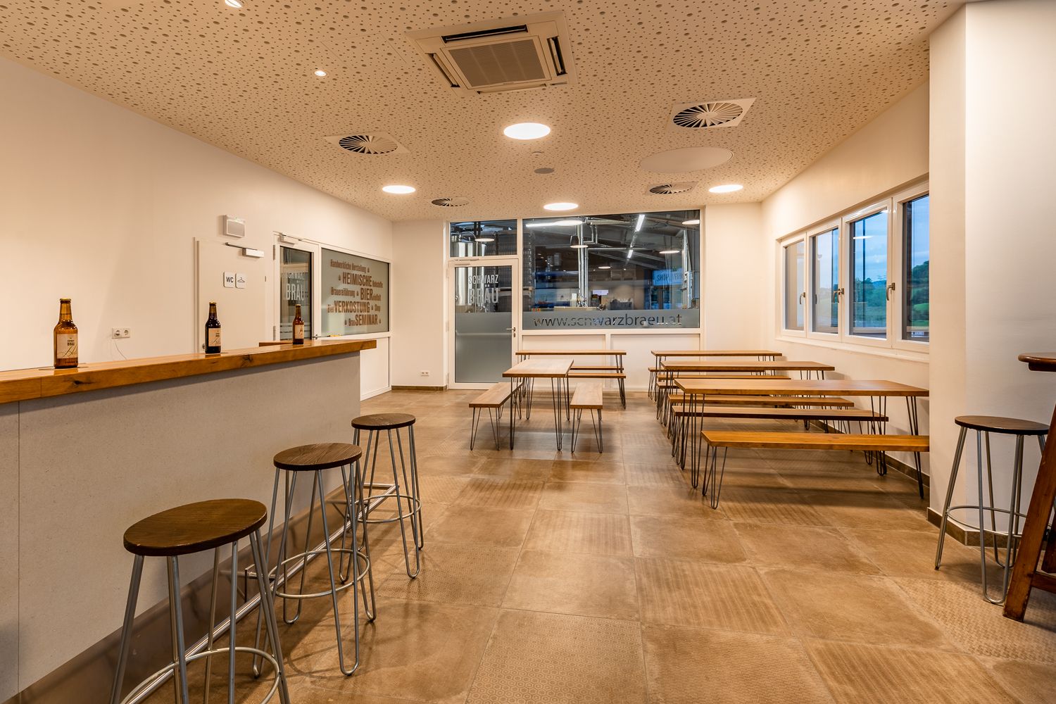 Tasting room of a brewery with wooden tables and benches and a bar with stools.