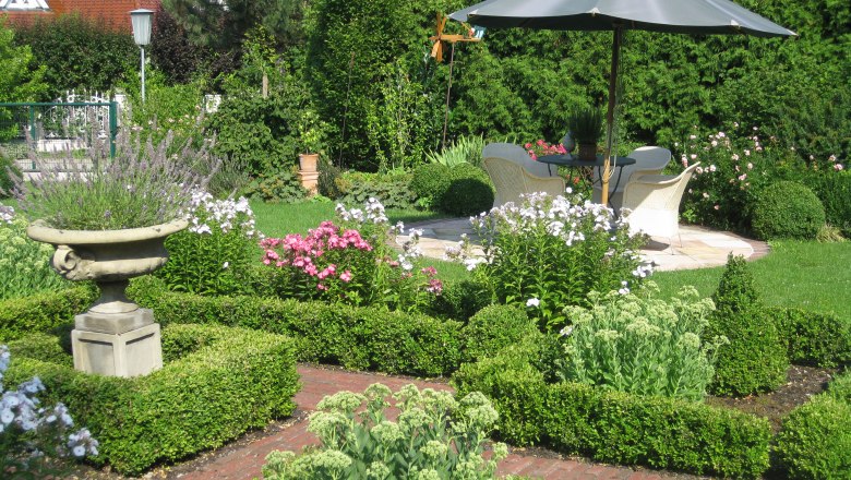 A well-tended garden with flower beds, a parasol and seating area.
