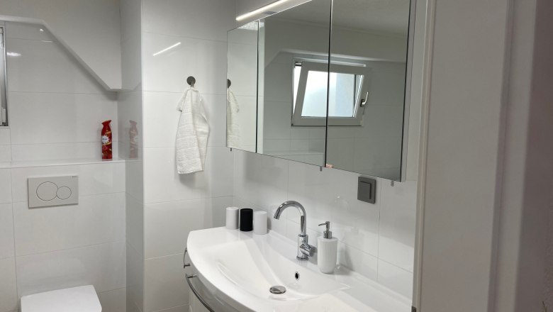 Modern bathroom with washbasin, mirror, toilet and small window.