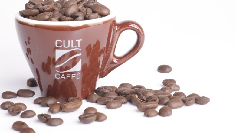 Brown cup with the inscription 'Cult Caffè', filled with coffee beans, on a white background.