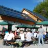 People sit at tables in front of a hut with solar panels and parasols.