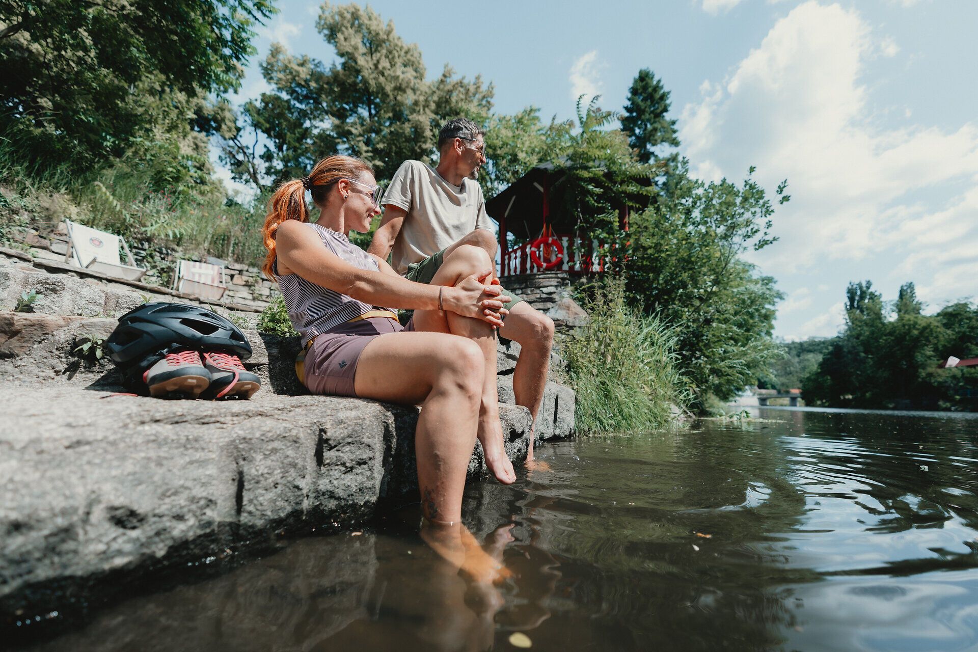 Two people sit on a stone staircase on the riverbank and cool their feet in the water.