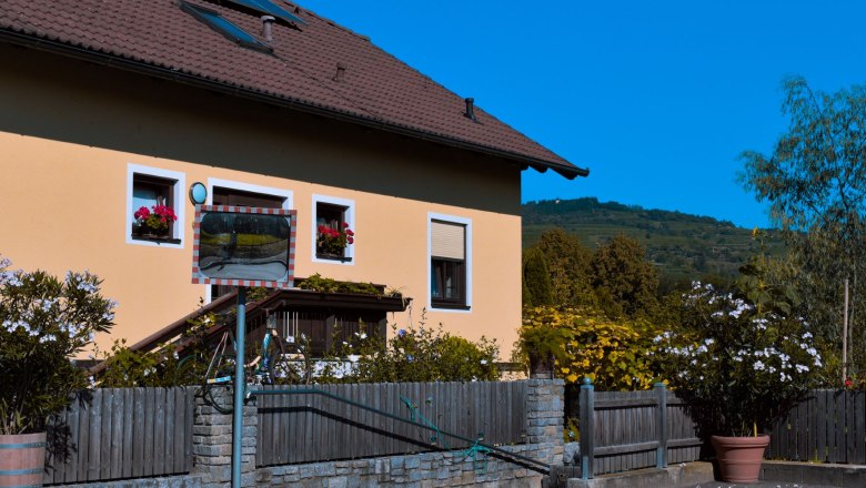 Exterior view of a house with a yellow façade, flowers in the windows and a traffic mirror in the foreground.