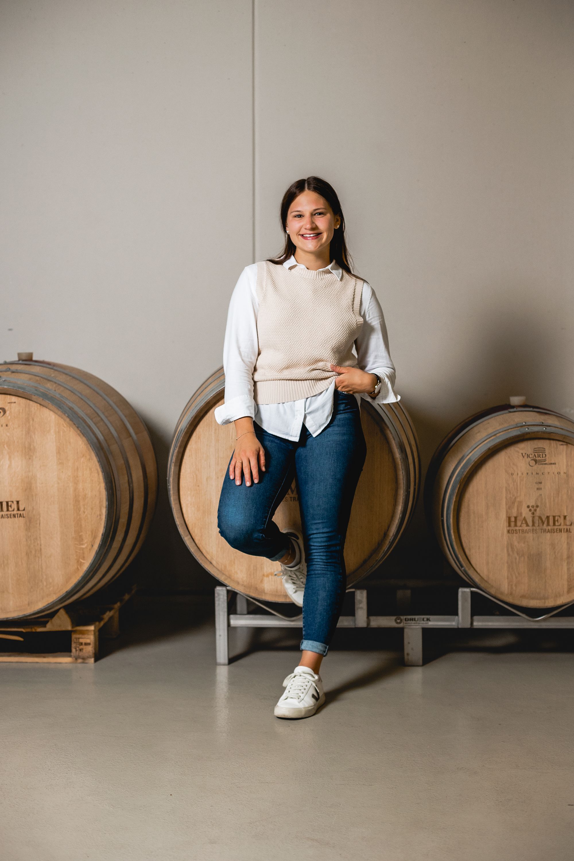 A woman leans smiling against a wine barrel at the Haimel winery.