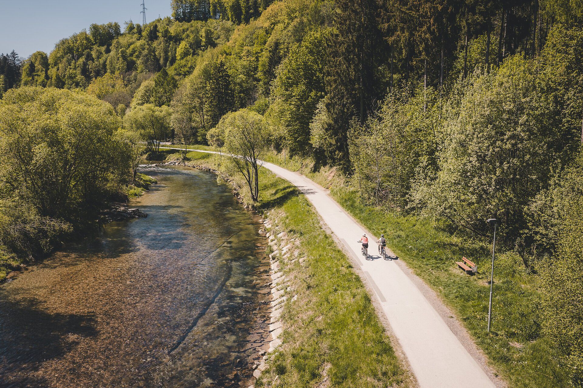 Two cyclists ride along the cycle path next to a river.