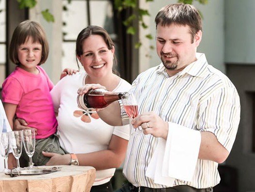 A man pours champagne into a glass while a woman and a child look on.