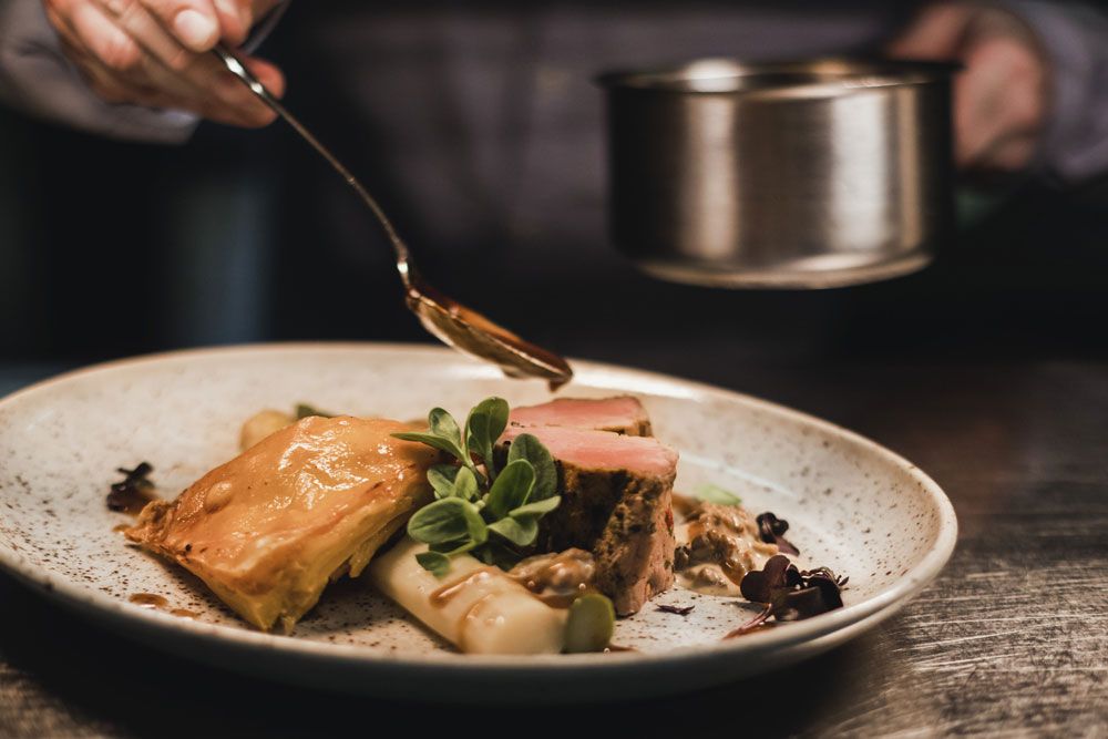 A plate of veal medallions, asparagus and puff pastry, garnished with sauce and herbs.