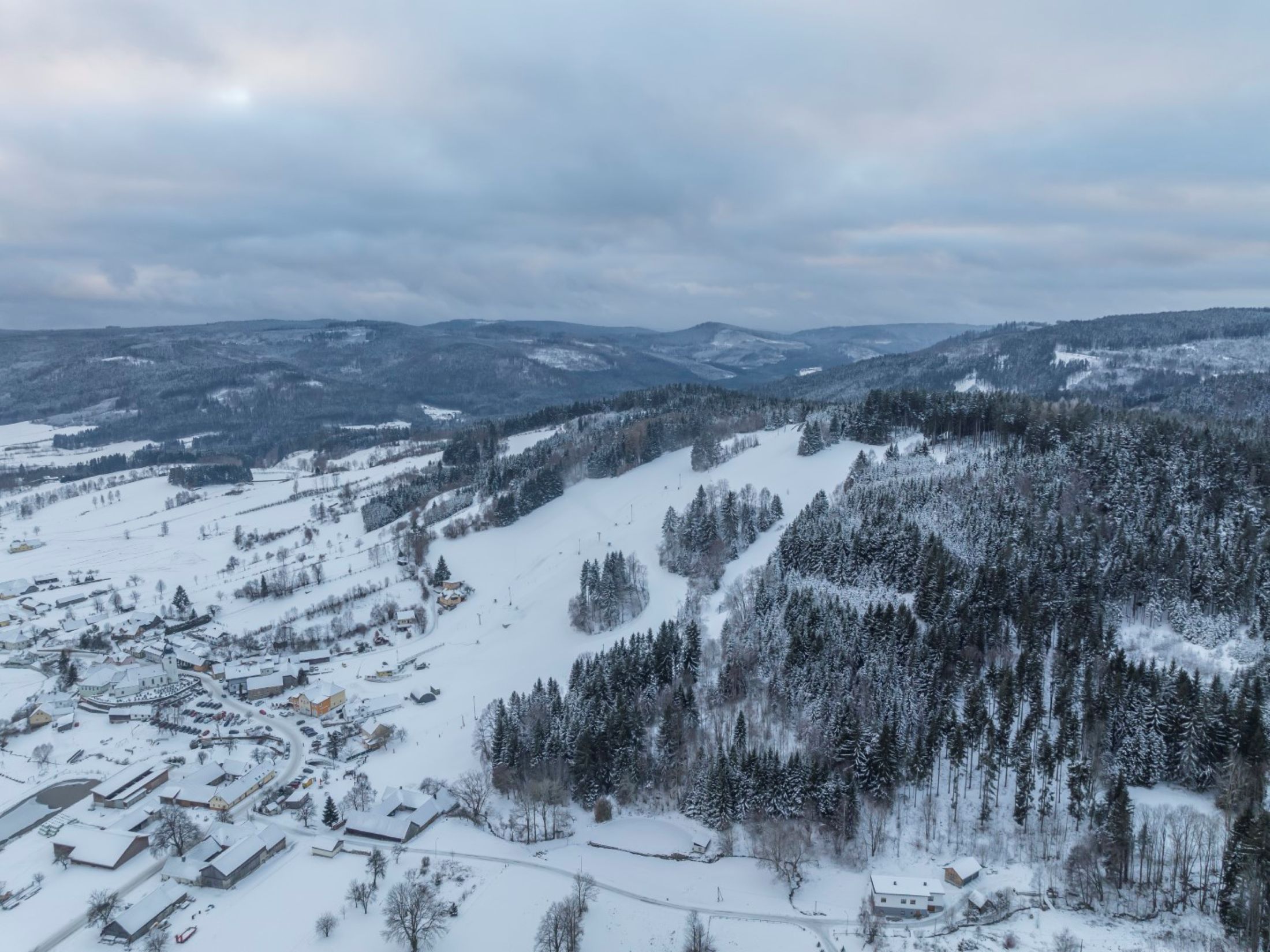 Aerial view of a snow-covered landscape with hills and forests.