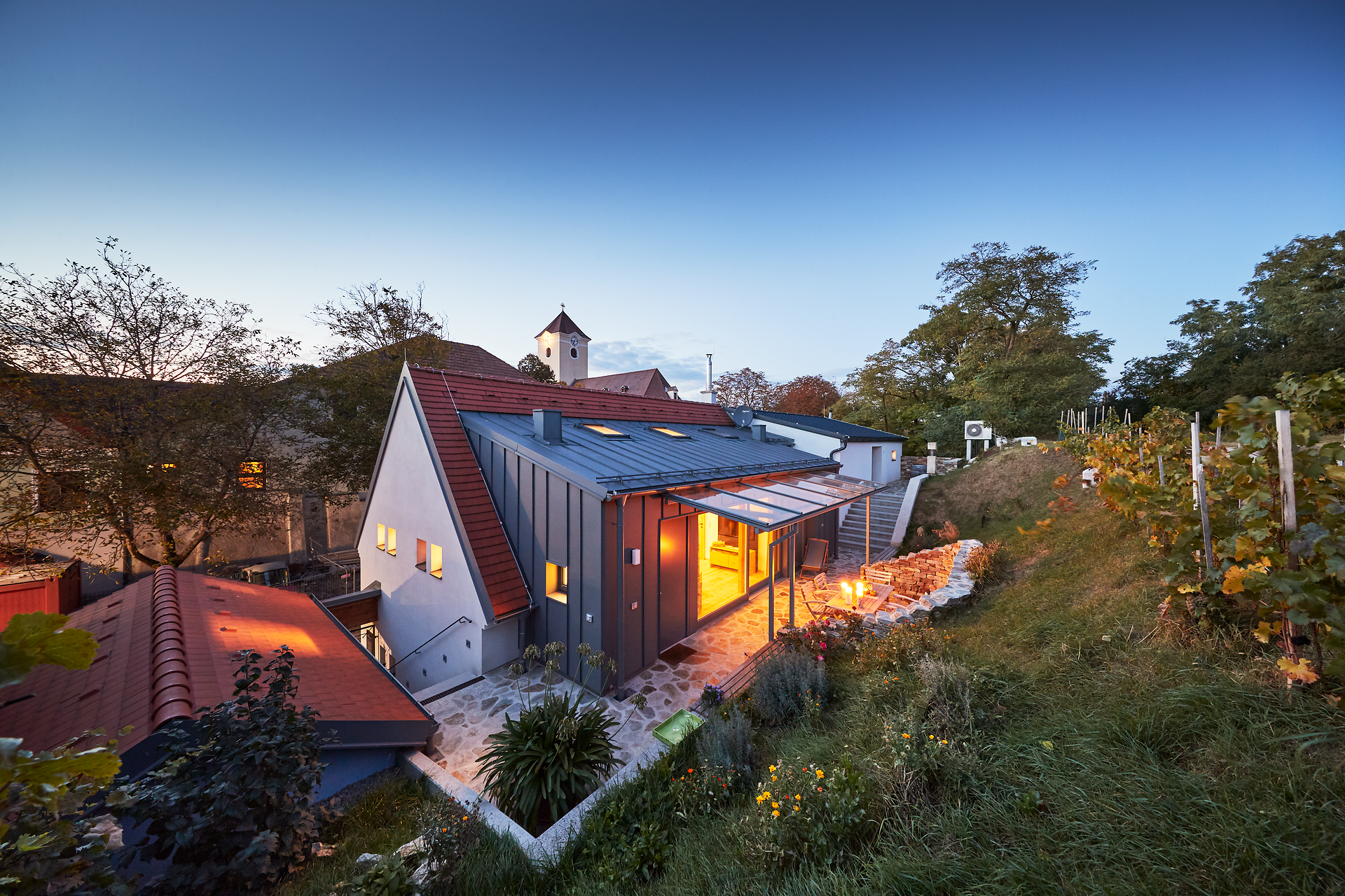 Winery with illuminated courtyard and vines in the foreground at dusk.