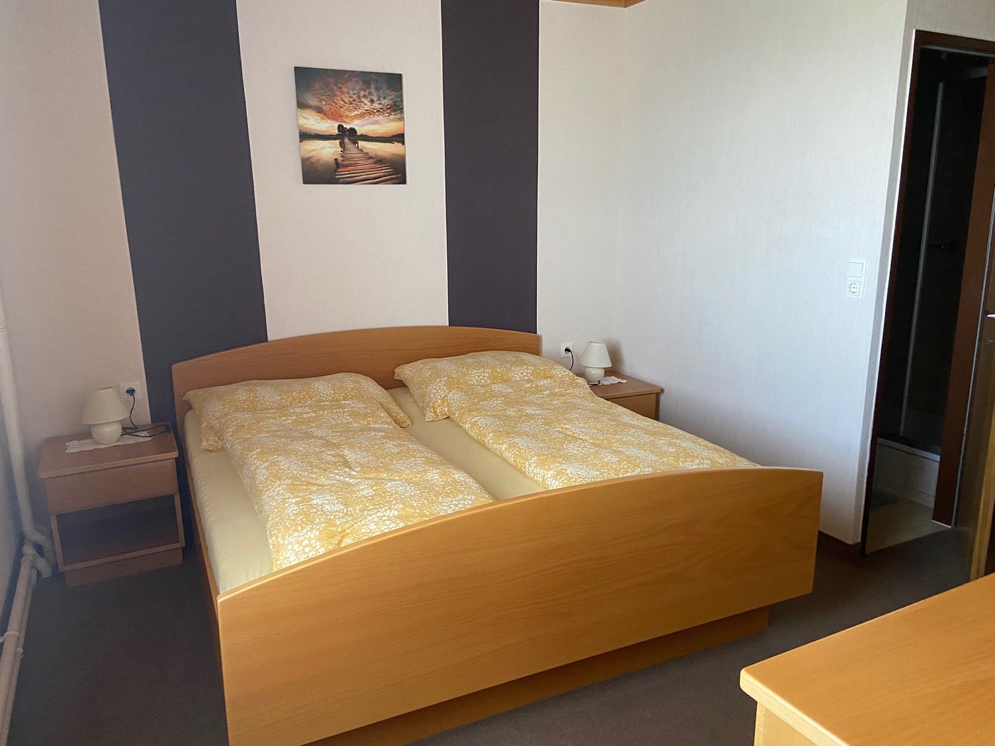 A double room with a wooden bed, two bedside tables and a picture on the wall.