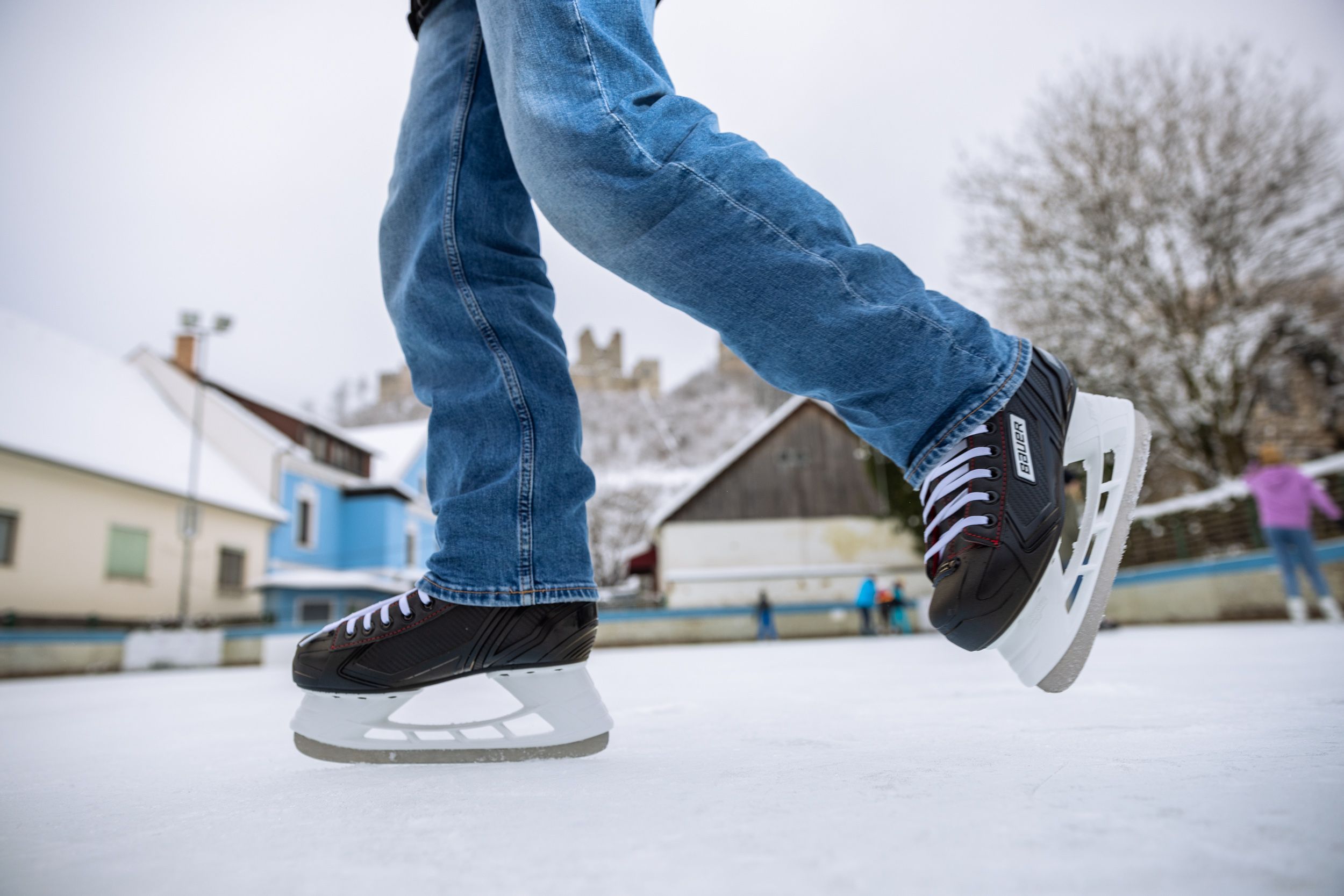 Close-up of ice skates on an ice rink with buildings and castle ruins in the background.