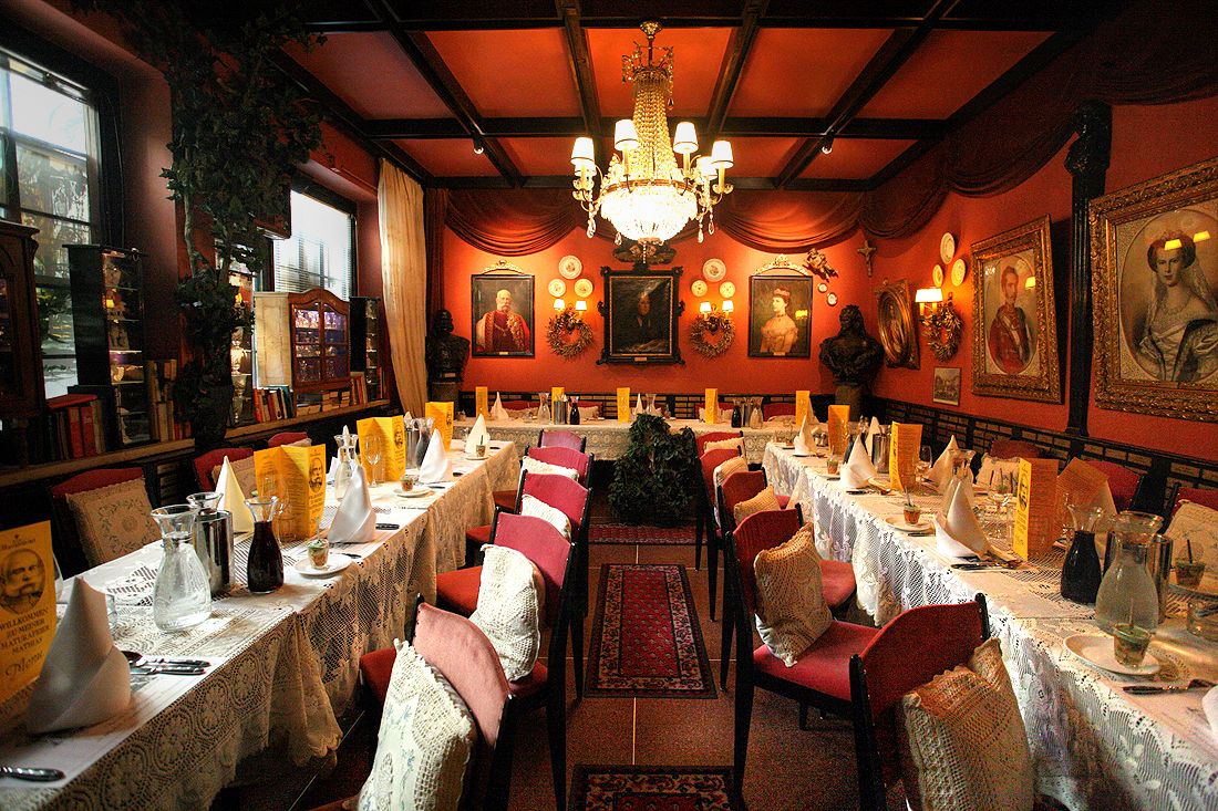 Elegant restaurant with long, laid tables, red walls and chandeliers.